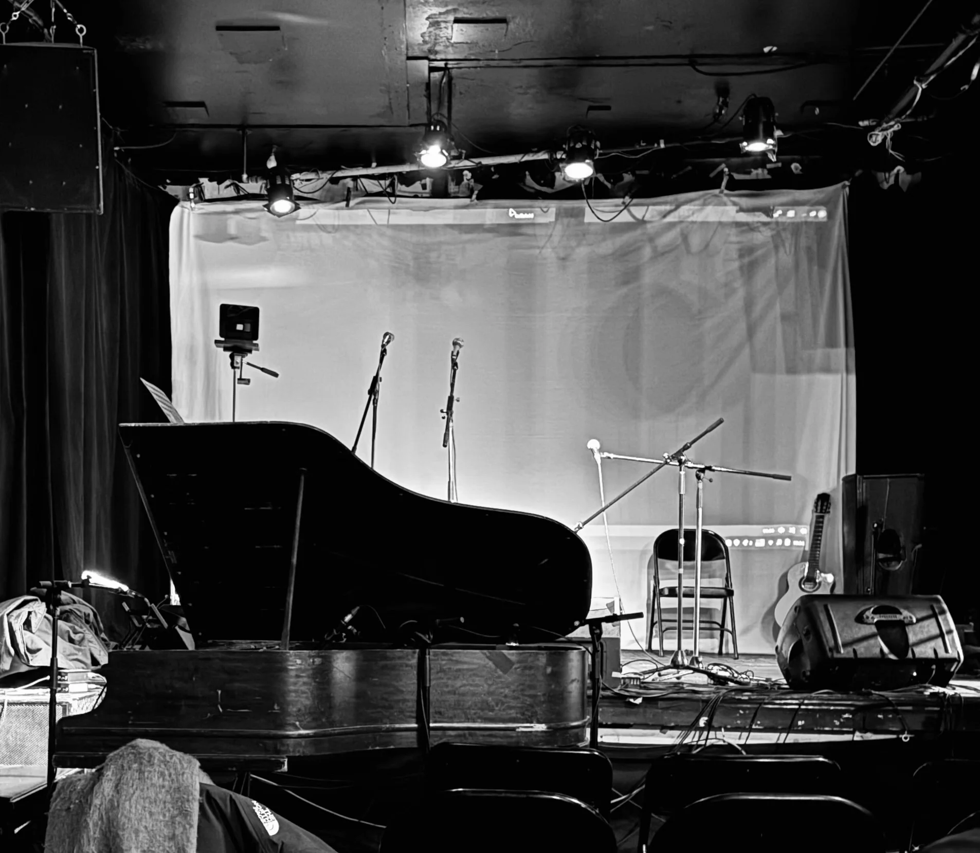 The empty stage at La Sotterenea, Montréal, in black and white — grand piano, microphones, one guitar